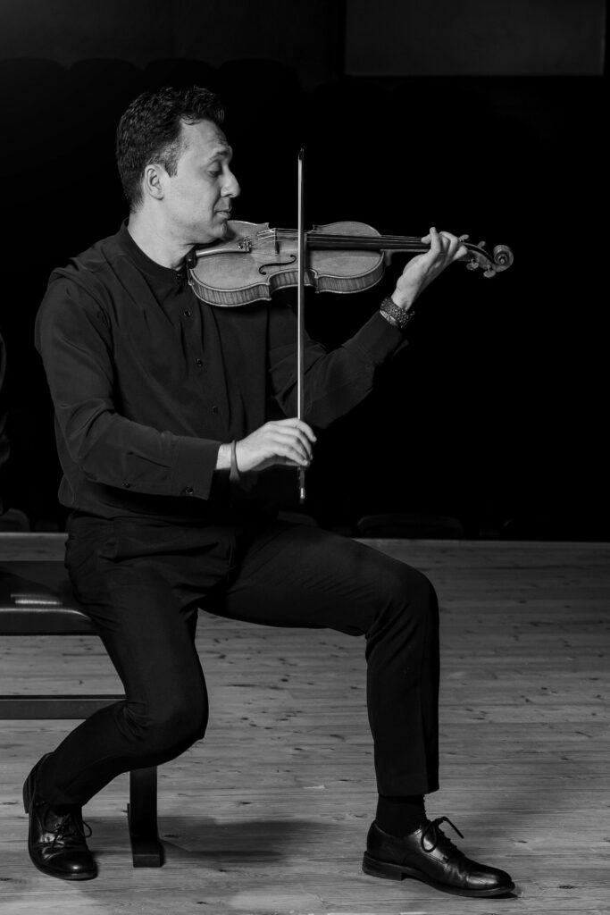 imagen en blanco y negro de Stefan Marinescu de perfil sentado en una silla tocando el violín con gesto de emoción en blanco y negro