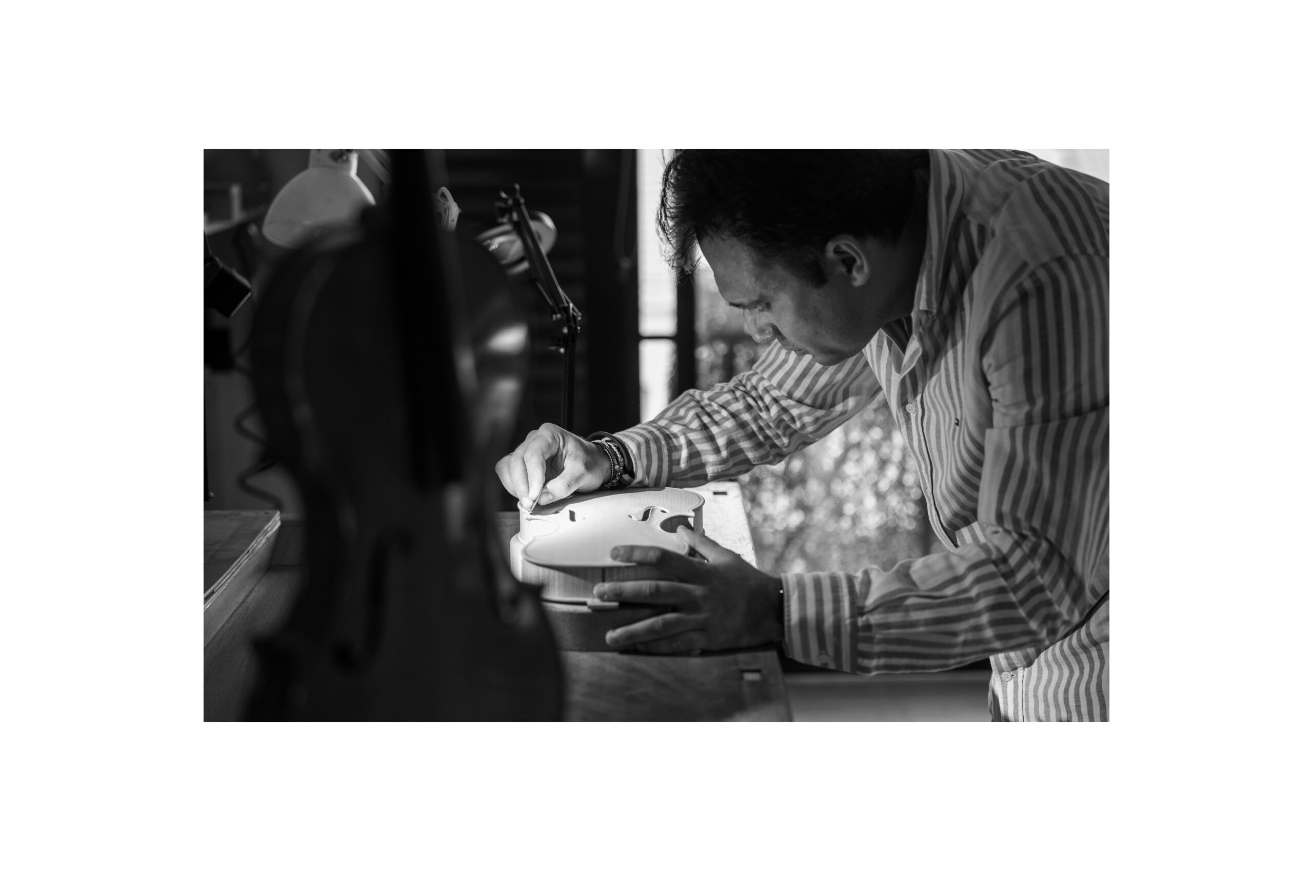 Stefan Marinescu concentrado trabajando en un violín sobre la mesa de su taller en blanco y negro