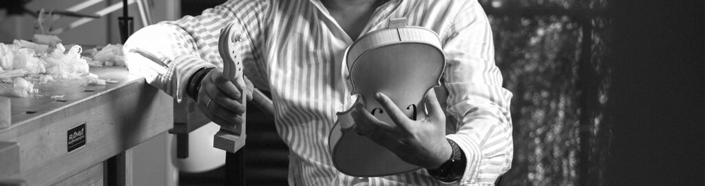 Stefan Marinescu sosteniendo un violín en desarrollo en las manos en su taller en blanco y negro