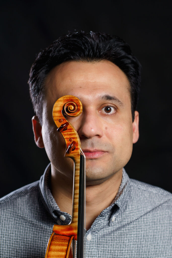 plano medio corto de Stefan Marinescu tapando uno de sus ojos con la voluta de uno de sus violines color marrón chocolate vista de perfil