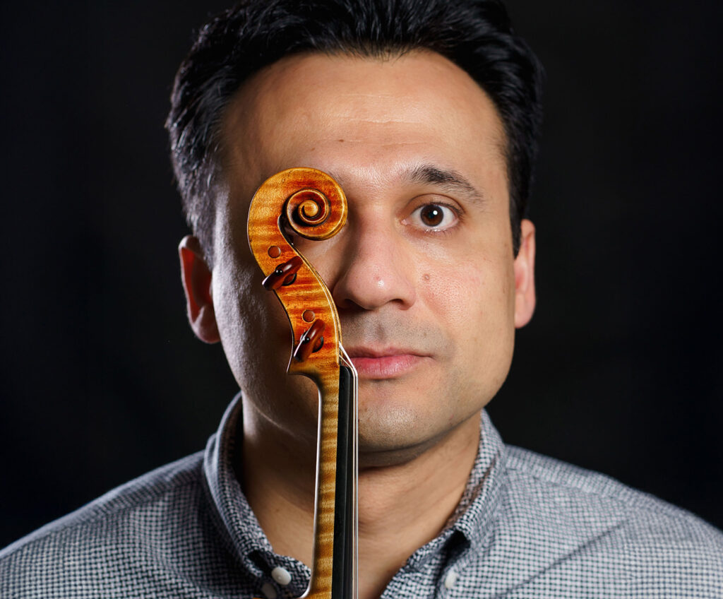 primer plano de Stefan Marinescu tapando uno de sus ojos con la voluta de uno de sus violines color marrón chocolate vista de perfil