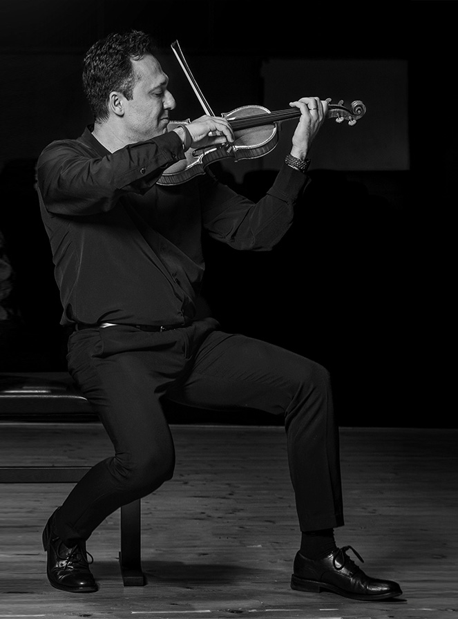 imagen en blanco y negro de Stefan Marinescu de perfil sentado en una silla tocando el violín con gesto de emoción en blanco y negro